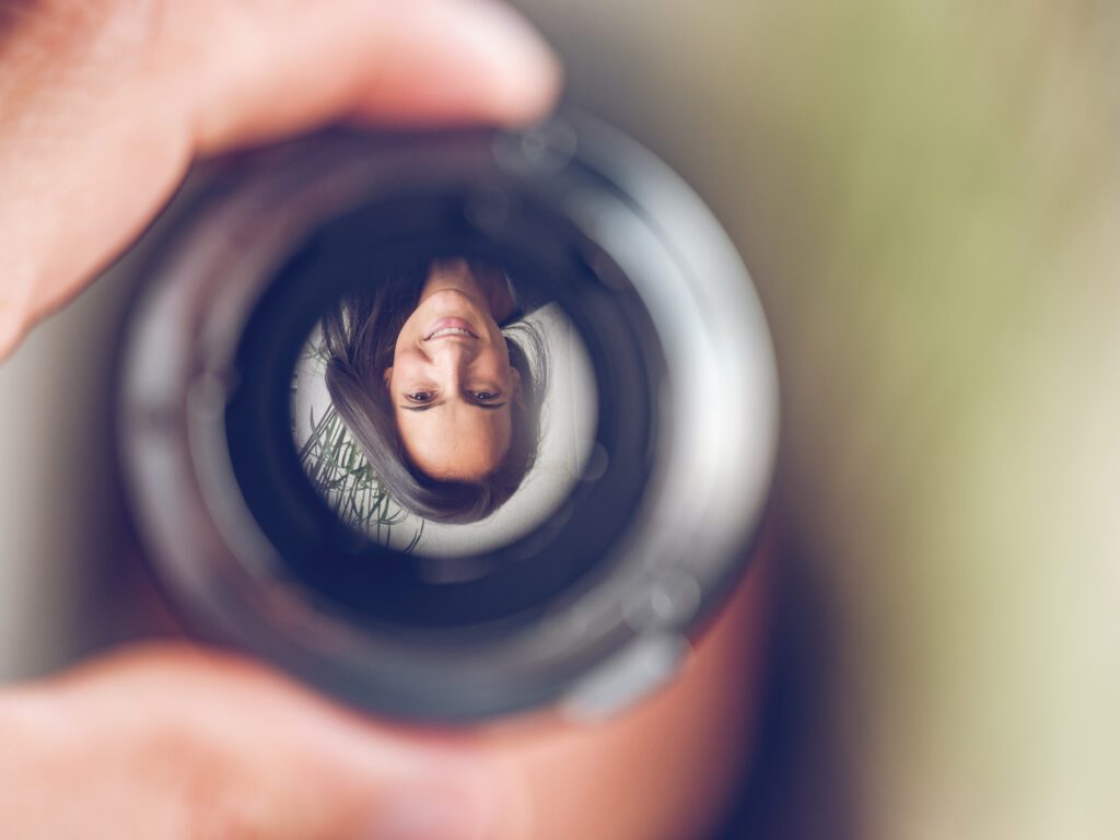 Change Perception: Closeup of crop hand holding lens with upside down reflection of smiling female with long dark hair looking at camera against blurred background